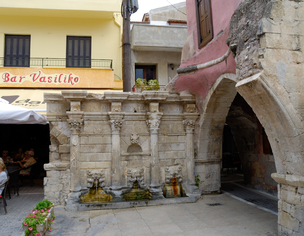 20.9. Rethymno, zauberhaftes Städtchen im Norden der Insel, der Rimondi-Brunnen Im ehemaligen Zentrum des venezianischen Retimo, am Nordende des Petychakis-Platzes (auch Platanos-Platz), befindet sich der erstmals 1588 erbaute Brunnen, der spätere Rimondi-Brunnen (????? Rimondi). Seinen Namen erhielt er vom Statthalter (Rettore ‚Rektor‘) Alvise Rimondi, der den Brunnen 1626 erneuern ließ. Öffentliche Brunnen dieser Art dienten einst der Wasserversorgung der Stadtbewohner. Zwischen den vier Säulen des Rimondi-Brunnens mit ihren korinthischen Kapitellen fließt Wasser aus drei Öffnungen in Form von Löwenköpfen in darunter befindliche Auffangbecken. Auf einem Fries oberhalb der Säulenkapitelle ist in lateinischen Buchstaben die fragmentierte Inschrift „… IACÆ LIBERALITATIS FONTES IN …“ zu lesen. Eine von den Osmanen über dem Brunnen errichtete Kuppel wurde im Zweiten Weltkrieg zerstört.